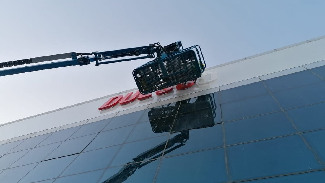 Boom lift installing red 3D letter signage on a glazed building facade