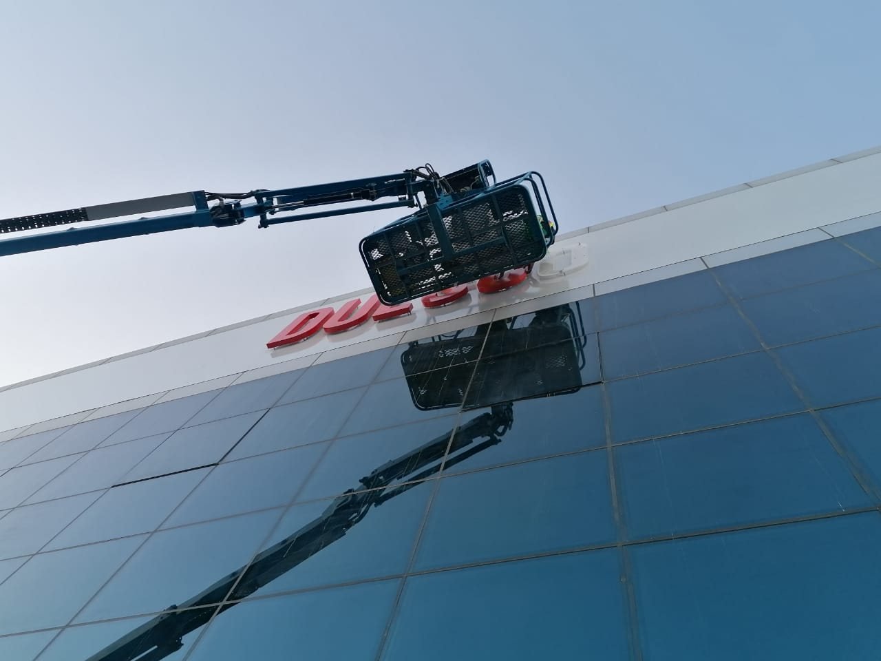 Boom lift installing red 3D letters on a glazed building facade