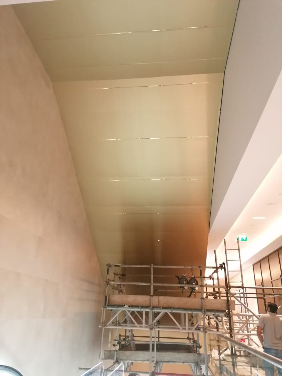 Gold-finish ceiling cladding panels being installed above an escalator